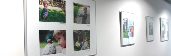 In einem Gang mit weißen Wänden hängen Bilderrahmen mit verschiedenen Fotos des Wettbewerbs 'Auf Augenhöhe'.