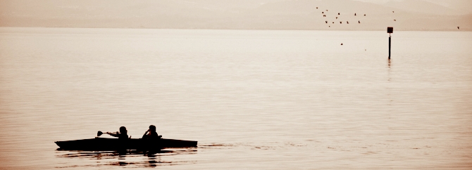 Zwei Personen sitzen in einem Kajak und paddeln gemeinsam über eine ruhige Wasserfläche.