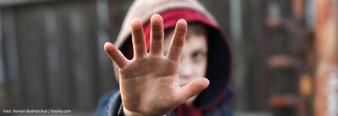 Ein armer Junge hält seine schmutzige Hand schützend vor sein Gesicht.