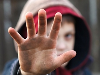 Ein armer Junge hält seine schmutzige Hand schützend vor sein Gesicht.