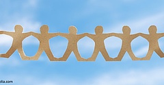 Symbolbild: Zwei Hände halten eine Menschenkette aus Papier gegen einen blauen Himmel.