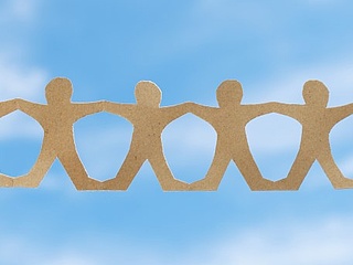 Symbolbild: Zwei Hände halten eine Menschenkette aus Papier gegen einen blauen Himmel.