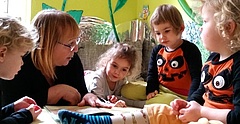 Tagesmutter Sylvia Zabel-Thäder, eine blonde, freundlich blickende Frau, sitzt zwischen den fünf Kindern, die sie in ihrer Kindertagespflegestelle in Leipzig betreut und bildet.
