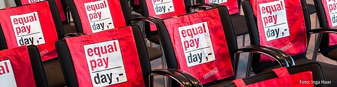 Auf den Rückenlehnen von Stühlen ist das Logo des Equal Pay Day abgebildet.