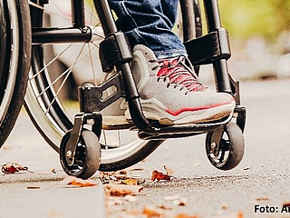 Die Räder eines Rollstuhls stehen am Bordstein einer Straße.