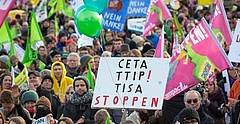 Viele Menschen mit bunten Fahnen und Schildern protestieren gegen die Freihandelsabkommen TTIP und CETA.