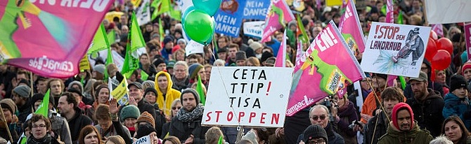 Viele Menschen mit bunten Fahnen und Schildern protestieren gegen die Freihandelsabkommen TTIP und CETA.