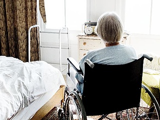 Eine ältere Dame sitzt im Rollstuhl und blickt aus dem Fenster. 