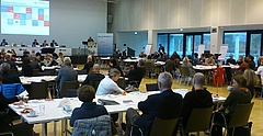 Mitgliederversammlung 2017 des Paritätischen Wohlfahrtsverbandes Sachsen, In einem großen Saal sitzen Menschen an Tischen. Im Hintergrund befindet sich ein Podium mit acht Personen sowie ein Rednerpult mit einem Redner.