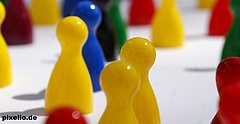 Spielfiguren verschiedener Farben stehen bunt vermischt auf einem weißen Untergrund. Sie symbolisieren Vielfalt, Miteinander und Integration.