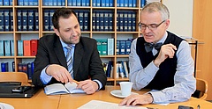 Zwei Männer sitzen an einem Tisch vor einer Wand mit Büchern und unterhalten sich. (Soziale Arbeit: Trägerkooperationen als Modell der Zukunft? Prof. Dr. Friedrich Vogelbusch im Gespräch mit Michael Richter)