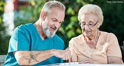 Ein Pfleger spricht mit einer älteren Dame über ihre Medikamente und sortiert diese in die kleinen Fächer eines Medikamentenhalters.