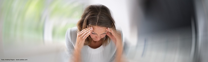 Symbolbild für eine Schmerz- oder Belastungssituation: Eine Frau halt ihre Hände an die Schläfen und um sie herum ist alles verschwommen. 