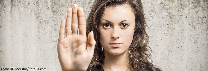 Eine brünette Frau hält ihre Handfläche den Betrachtenden entgegen und signalisiert dadurch ein klares Stopp.