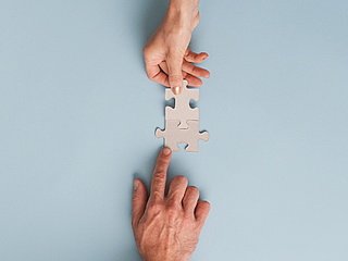Symbolbild: Zwei Hände fügen zwei Puzzleteile zusammen.