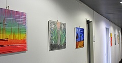 Blick auf die Ausstellung des ASB Chemnitz im den Gang der Landesgeschäftsstelle des Paritätischen Sachsen in Dresden. Bunt bemalte Leinwände hängen an der Wand.