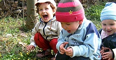 Drei Kinder spielen im Garten und freuen sich über eine Entdeckung im Gras. Kindertagespflege Sachsen