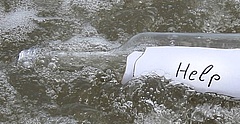 Eine Flaschenpost mit einem Zettel auf dem Hilfe steht, liegt in der Brandung eines Strandes.