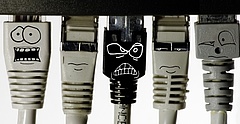 Internetsicherheit: Fünf Lan-Stecker sind an einem Computer angebracht. Jeder Stecker hat ein Gesicht. Der mittlere Stecker ist schwarz und hat eine böse Grimasse.