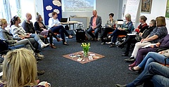 Menschen sitzen in einem Stuhlkreis und hören einem Redner zu.