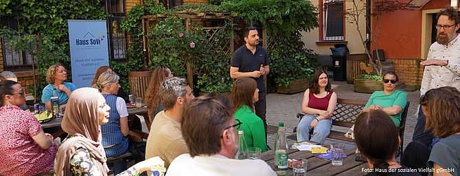 Menschen sitzen an einem sonnigen Tag im Hof des Hauses der sozialen Vielfalt in Leipzig und sprechen miteinander.